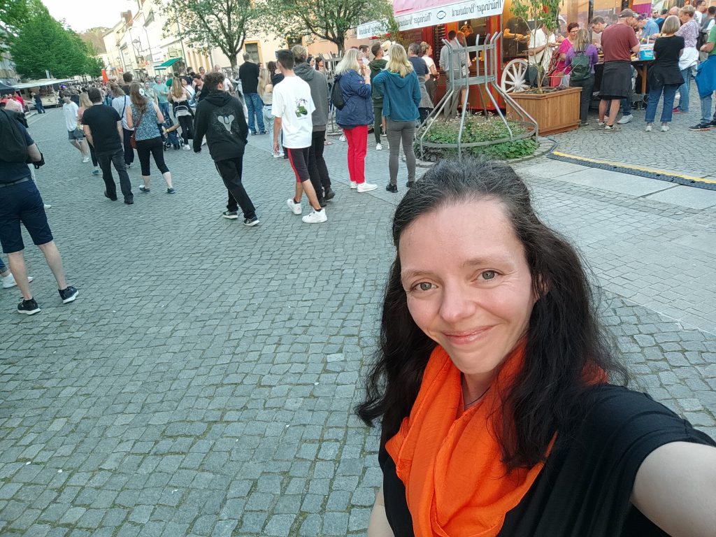 Selfie Nadine Schnittke mit orangem Tuch, Hintergrund Menschen