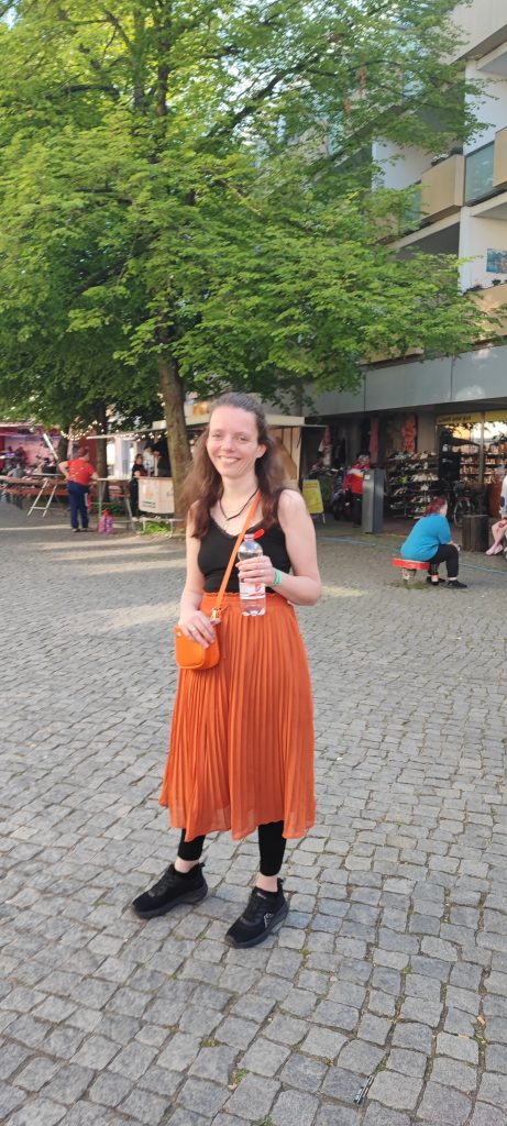 Nadine Schnittke mit orangem Rock und Wasserflasche in der Hand in der Bürgermeisterstraße