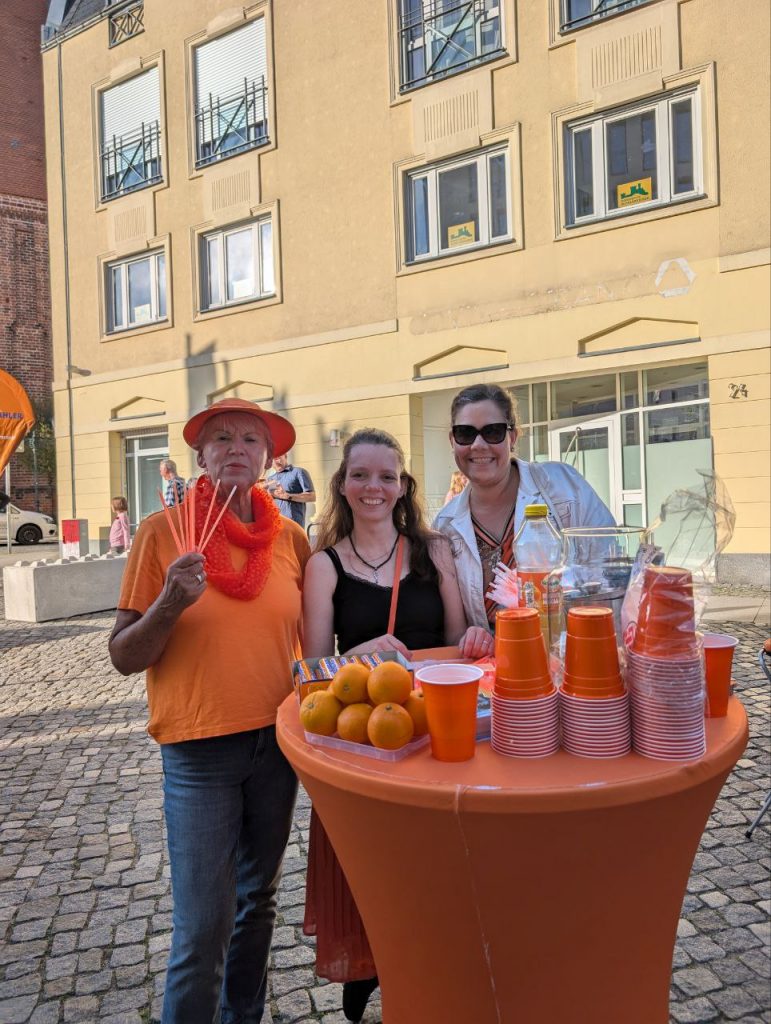 Christiane Strese, Nadine Schnittke und Julia Schmitz stehen am Tisch mit Werbematerial und Orangen